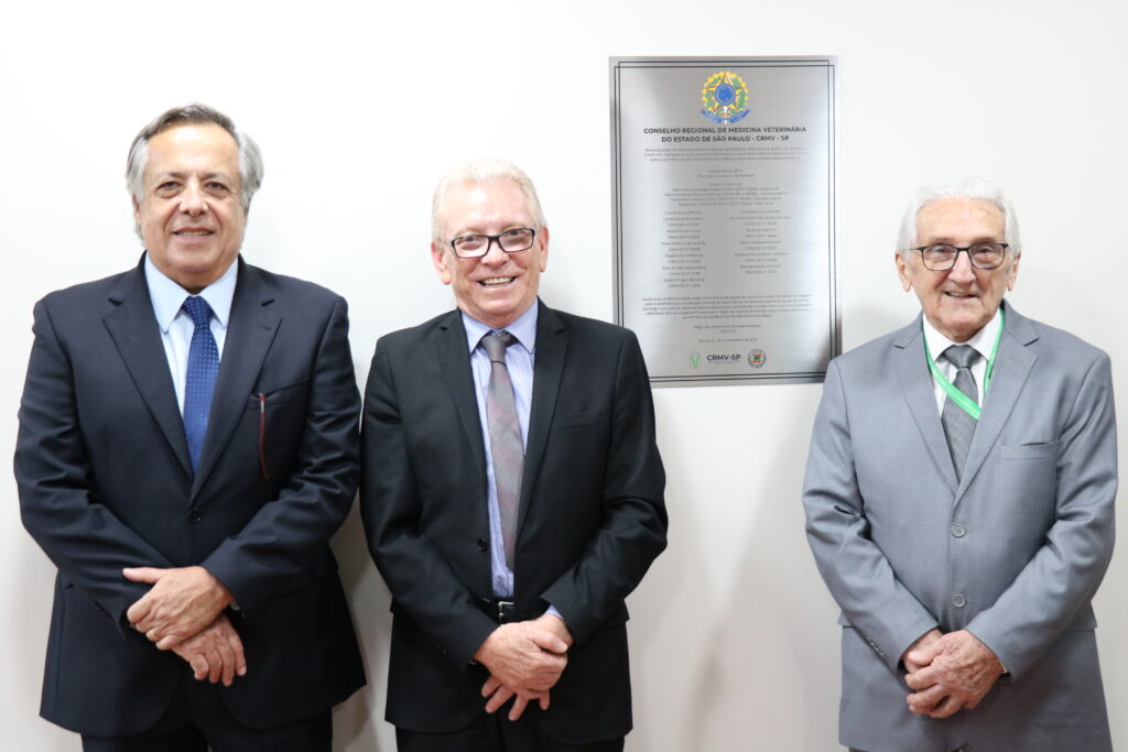 A foto mostra os três presidentes do CRMV-SP, da atual gestão e das gestões anteriores, ao lado da placa do CRMV-SP.
