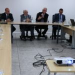 Visão parcial da sala mostra oito presidentes de comissões, o presidente do CFMV, e o presidente do CRMV-SP. Todos estão sentados e atentos a fala do presidente do CRMV-SP, que segura um microfone.