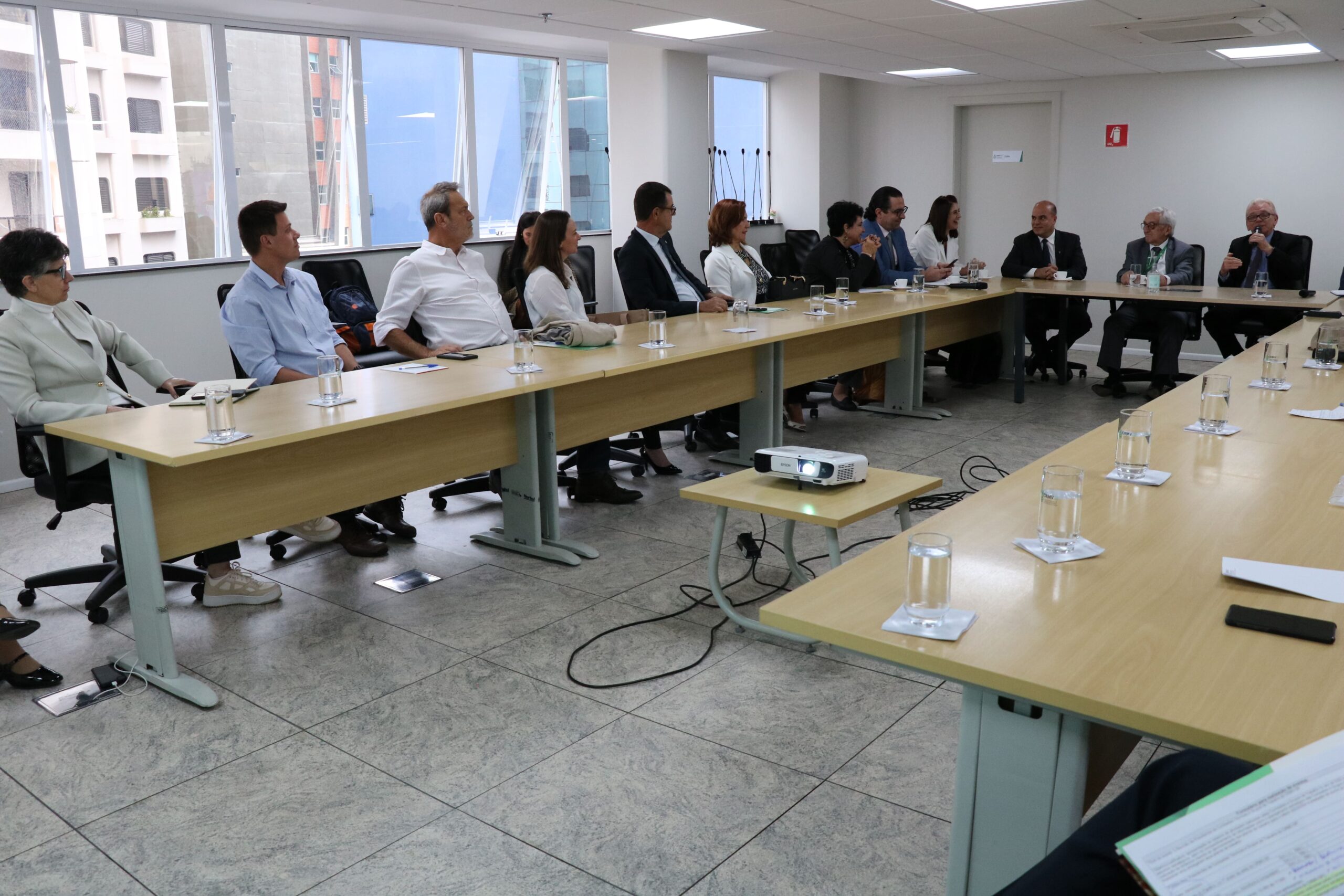 Visão lateral da sala. Em que é possível ver os presentes em dois dos lados do "U" formado pela disposição das mesas. No canto direito da imagem, o presidente do CRMV-SP fala do microfone.