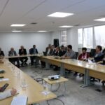 Sala ampla com mesas na cor bege dispostas em formato de "U". Ao entorno estão sentados presidentes de comissões, coordenadores e membros da diretoria do CRMV-SP, bem como o presidente do CFMV. Todos estão atentos a fala do presidente do Regional, o qual seria o microfone.