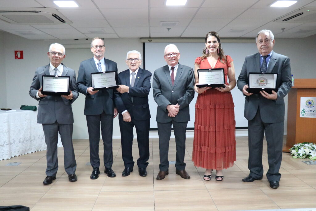 Seis pessoas, sendo uma mulher e cinco homens. Eles posam para a foto para comemorar os prêmios recebidos. A mulher e três homens seguram placas nas mãos.