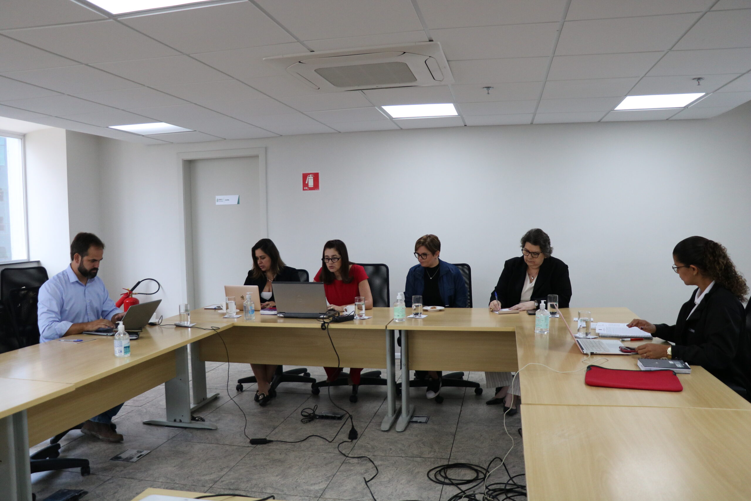 Cinco mulheres e um homem sentados à mesa, trabalhando em notebooks.