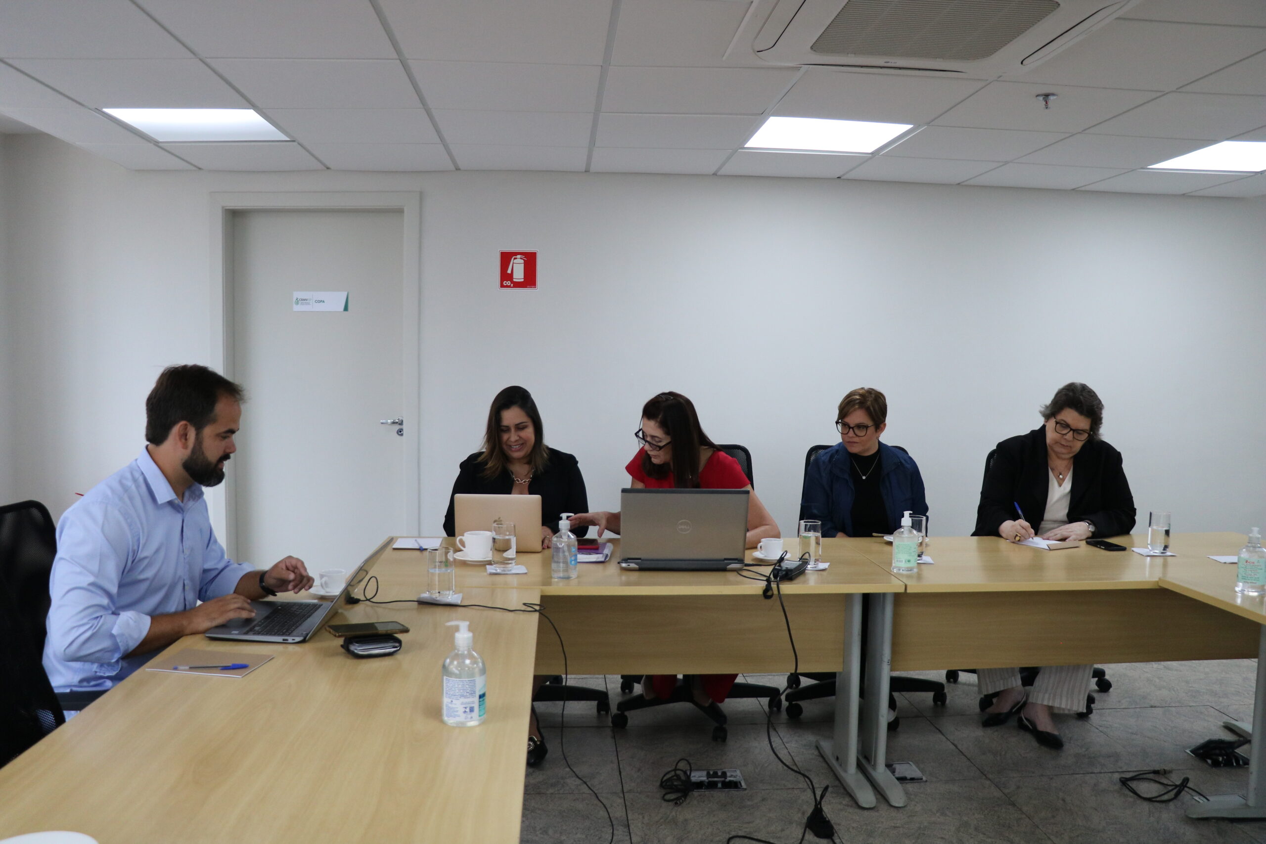 Quatro mulheres e um homem sentados à mesa de trabalho, com notebooks.