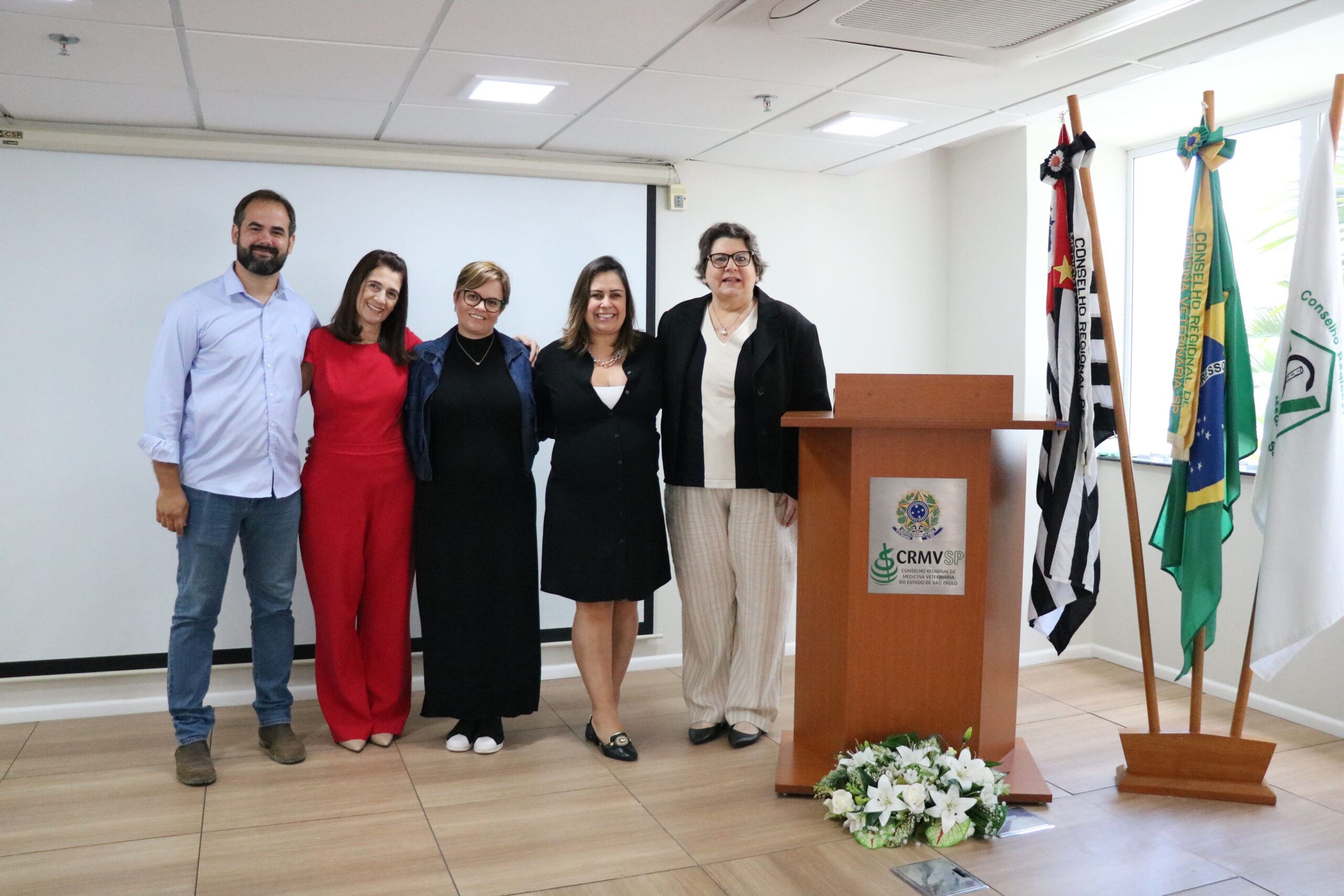 Cinco pessoas, sendo um homem e quatro mulheres, em pé, lado a lado, posando para a foto.