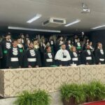 A imagem mostra os alunos de graduação no palco, vestidos com beca.