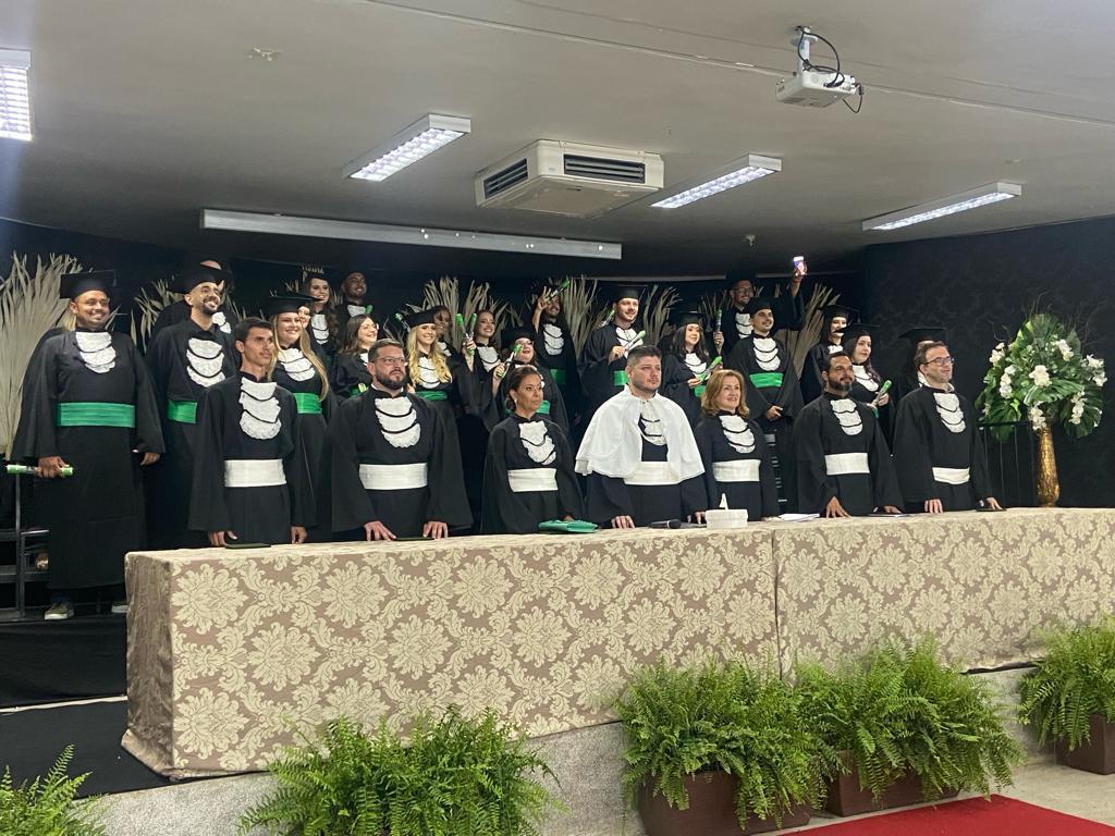 A imagem mostra os alunos de graduação no palco, vestidos com beca.