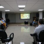 Na foto, sessão do Grupo de Apoio Mútuo. Os participantes estão sentados em cadeiras em círculos. Ao fundo, telão com explicação sobre as emoções.