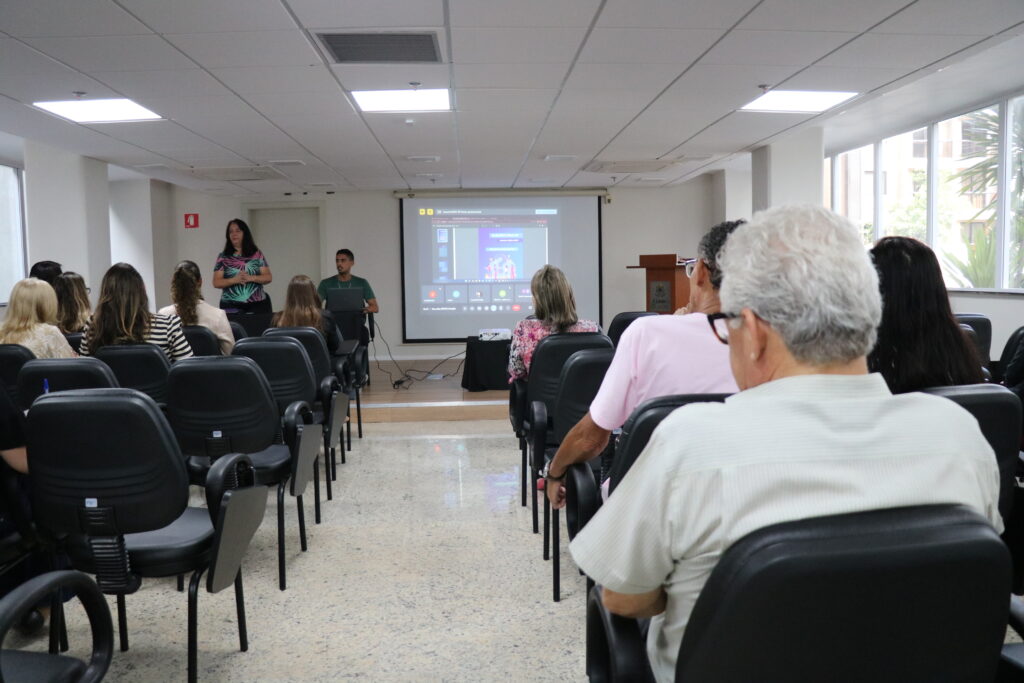 Na foto, aparecem colaboradores do CRMV-SP durante treinamento para as eleições do órgão. Eles estão sentados e aparecem de costas, viradas para a apresentadora, que está ao lado de um telão com a apresentação.