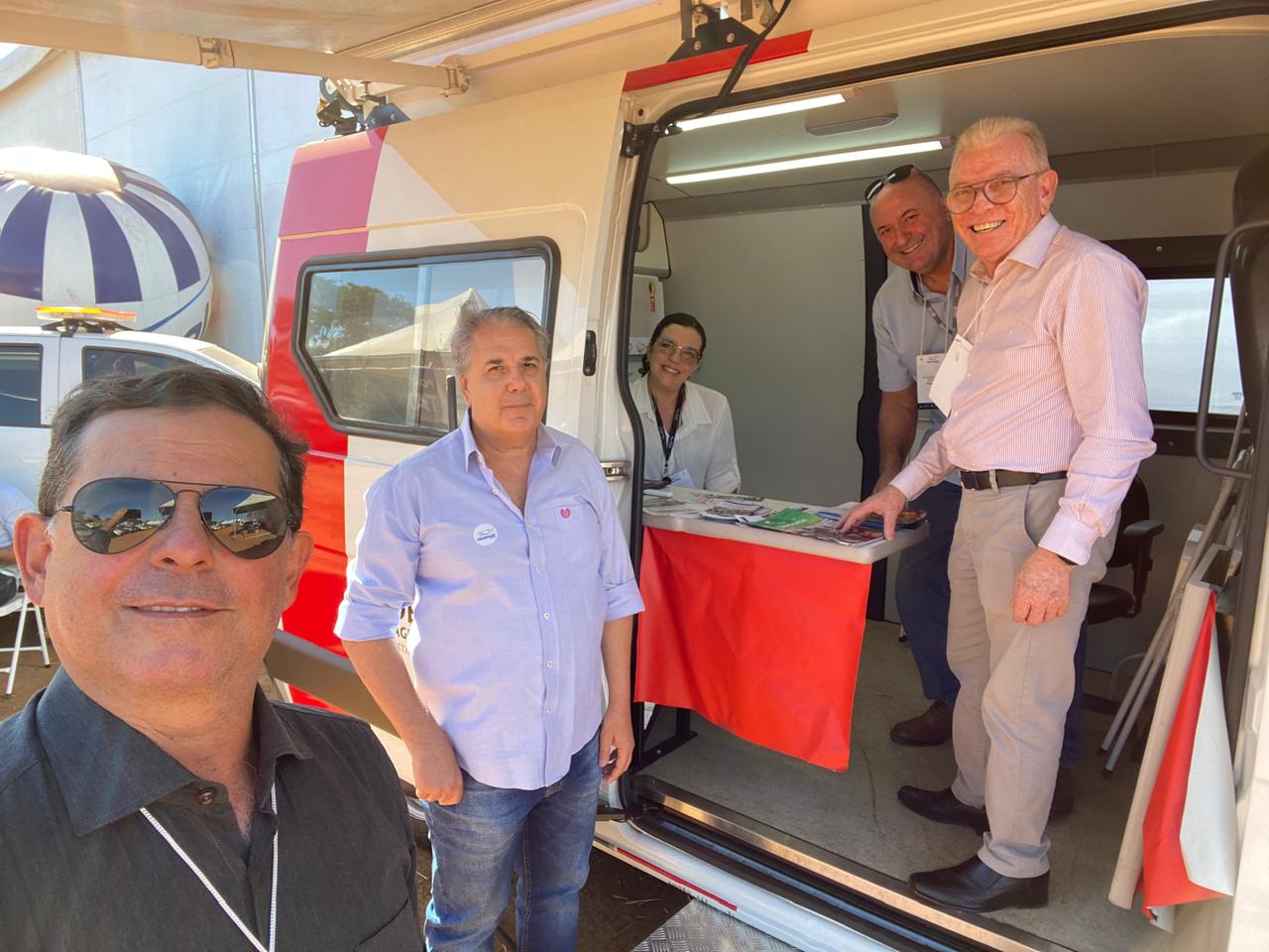Quatro homens em pé e uma mulher sentada em carro de atendimento do evento.