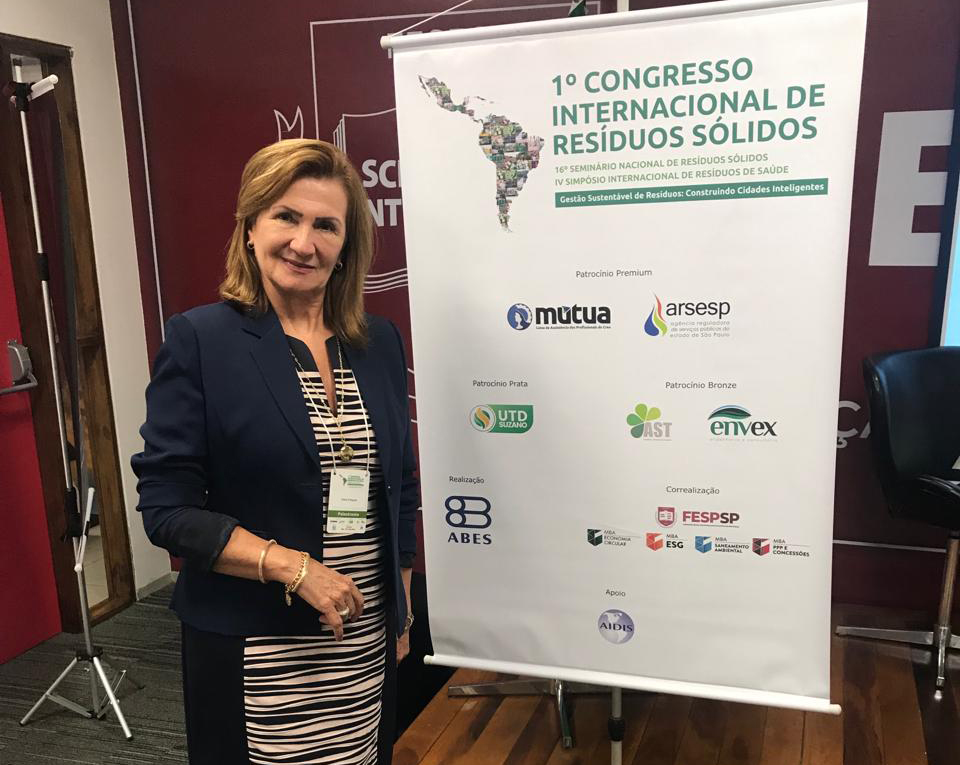 Presidente da Comissão de Saúde Ambiental do Conselho Regional de Medicina Veterinária do Estado de São Paulo, Elma Polegato, está ao lado de banner do 1o Congresso Internacional de Resíduos Sólidos.