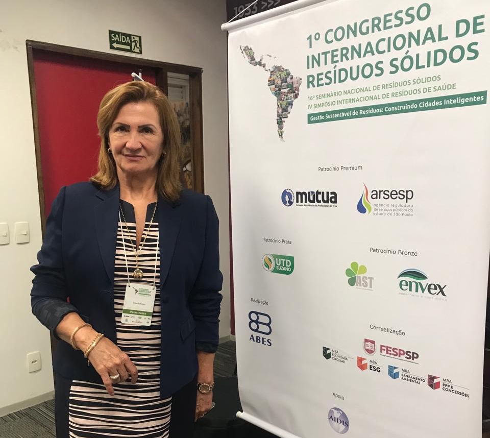 Presidente da Comissão de Saúde Ambiental do CRMV-SP, Elma Polegato, está ao lado de banner do 1o Congresso Internacional de Resíduos Sólidos.