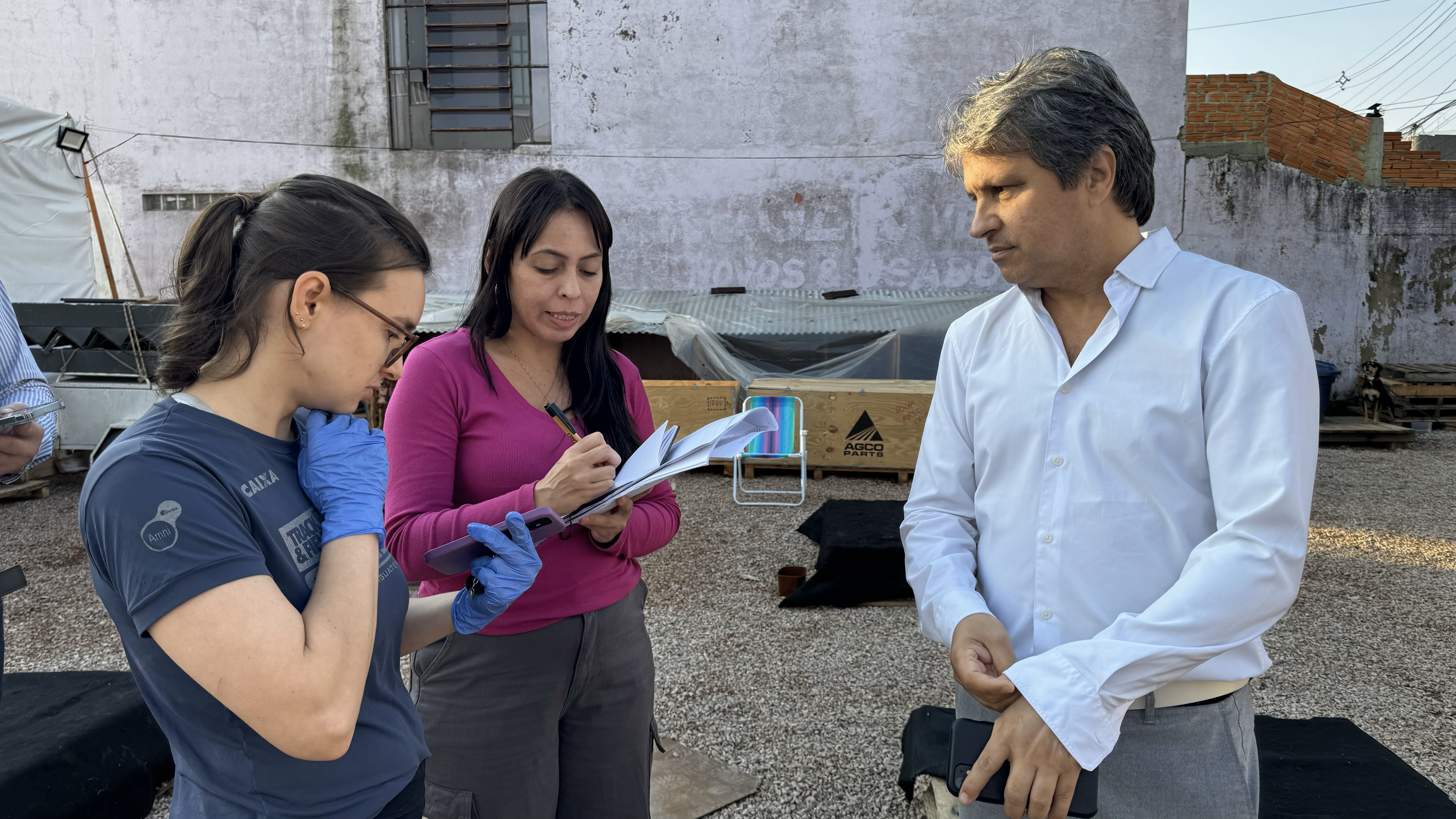 Duas mulheres e um homem em pé passando dados para um caderno.