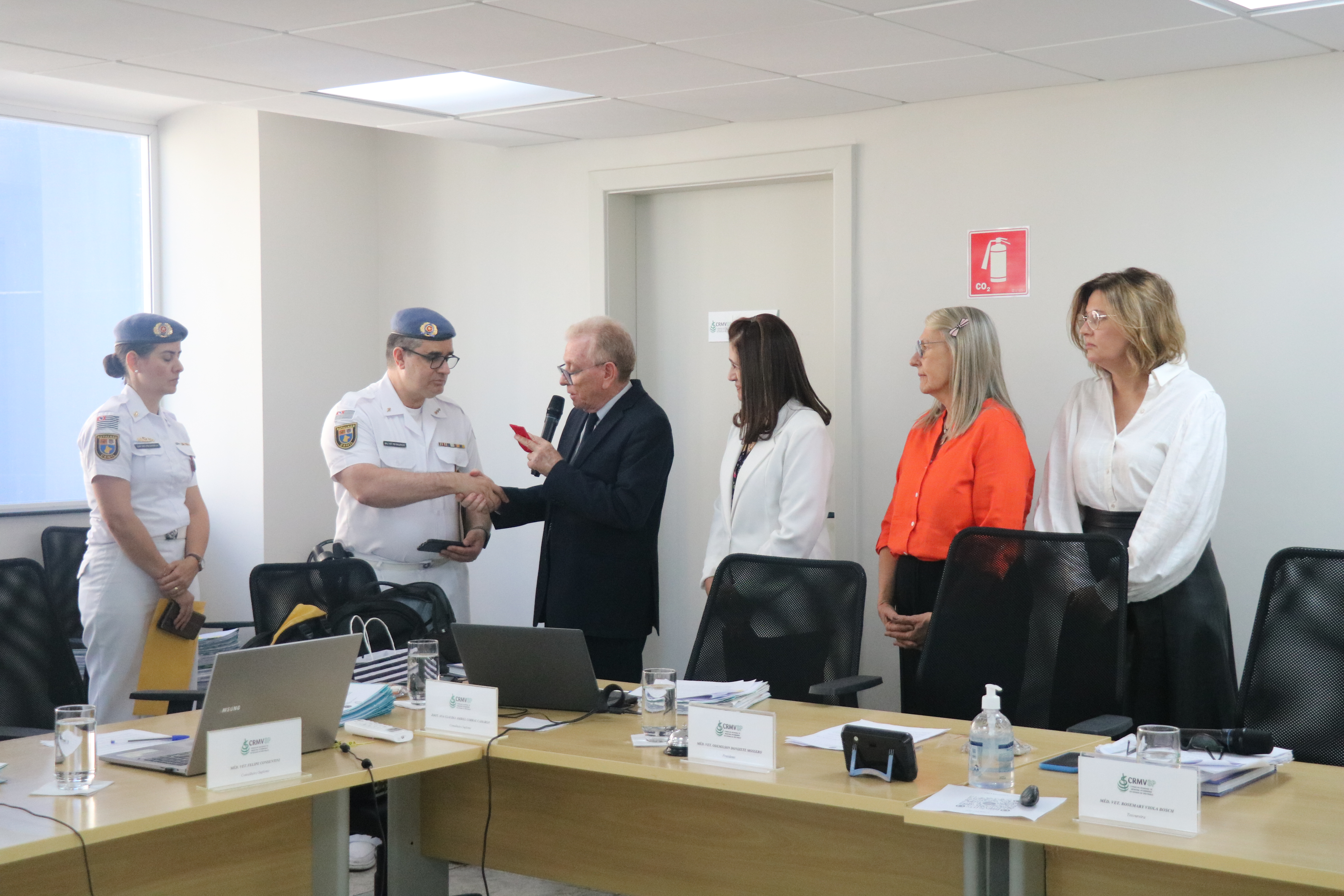Visão lateral direita dos médicos-veterinários(uma mulher e um homem) militares recebendo medalha de homenagem do presidente do CRMV-SP.