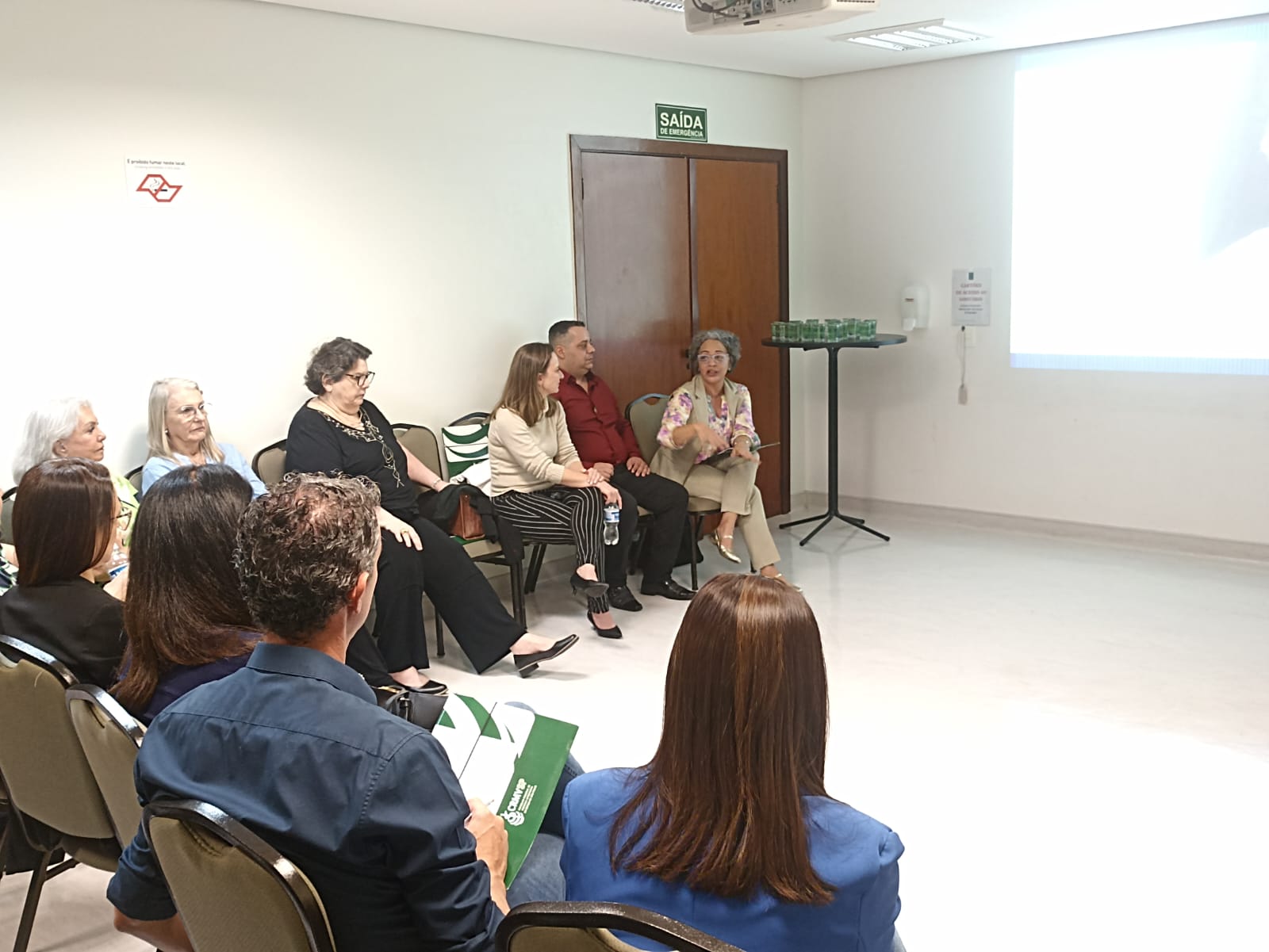 Pessoas sentadas em semicírculo durante reunião do Grupo de Apoio Mútuo(GAM) ouvindo palestrante.