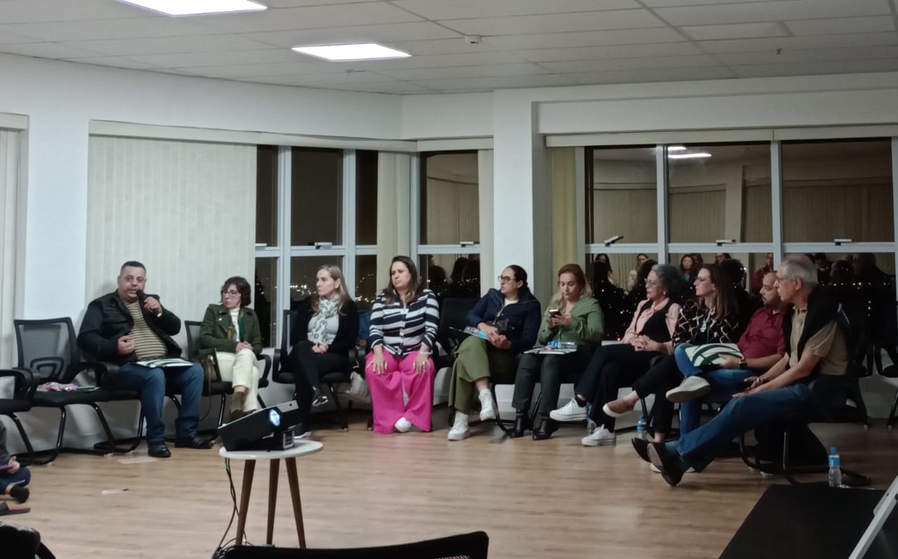 Pessoas sentadas em semicírculo em sala de treinamento.