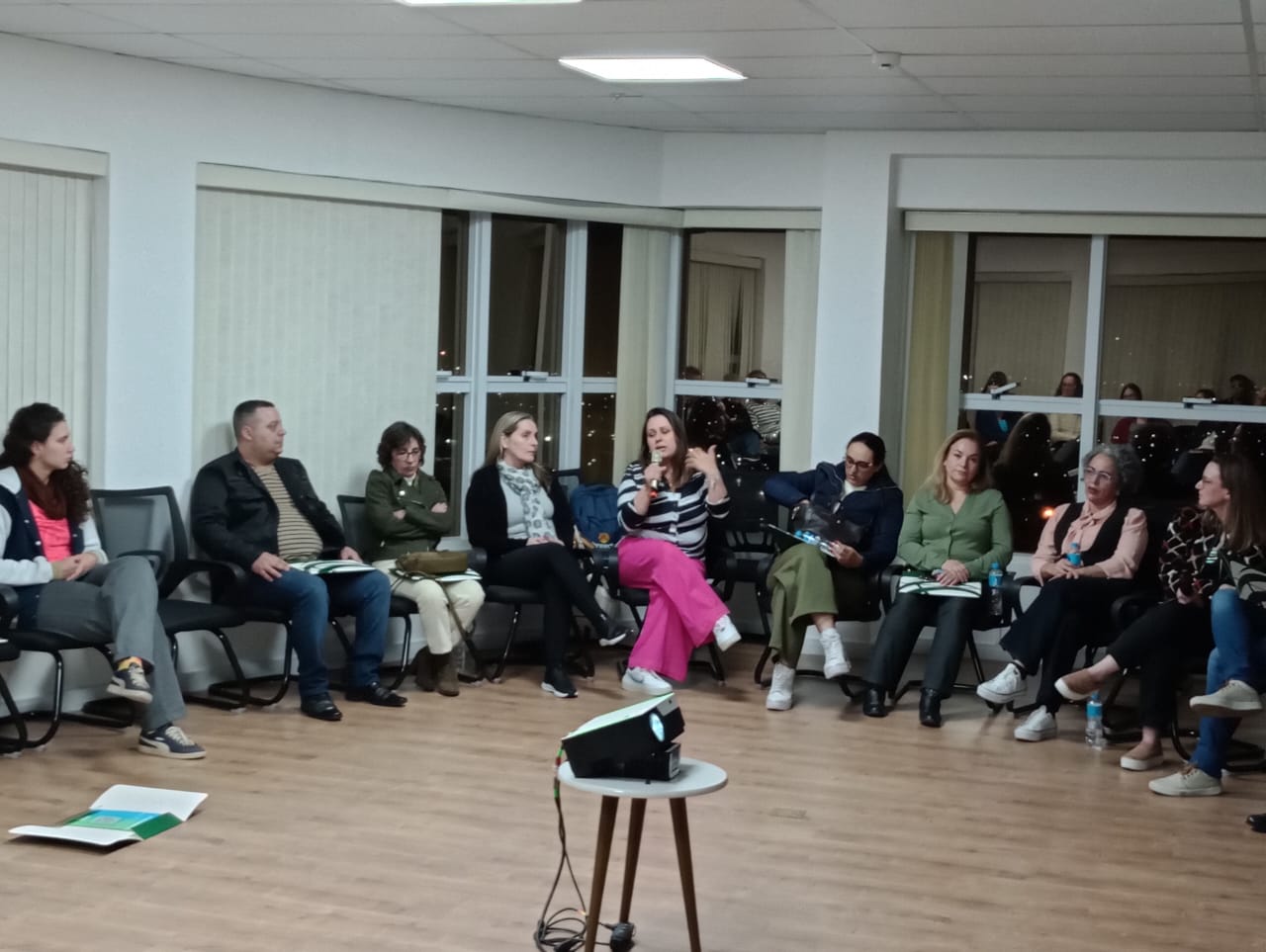Pessoas sentadas em semicírculo em sala de treinamento.