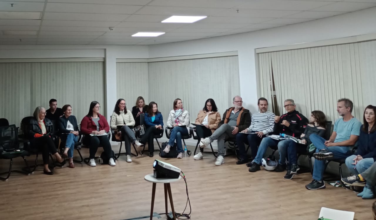 Pessoas sentadas em semicírculo em sala de treinamento.
