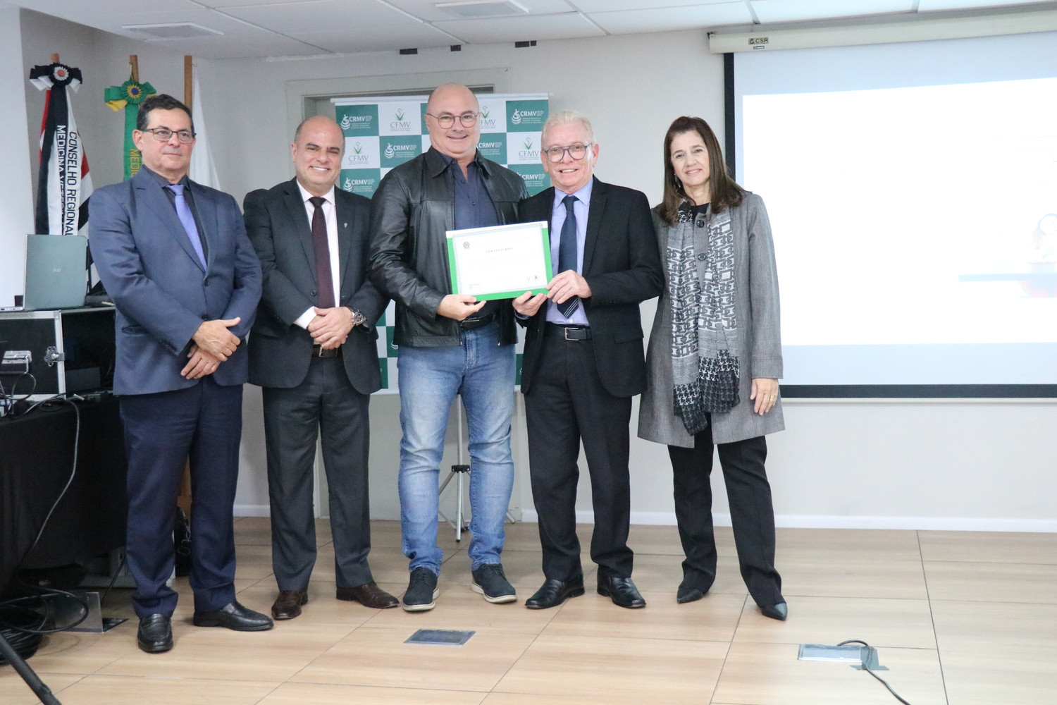 No palco, os membros da Diretoria Executiva do CRMV-SP posam ao lado de um presidente de Comissão Técnica homenageado com certificado em reconhecimento ao trabalho desempenhado.
