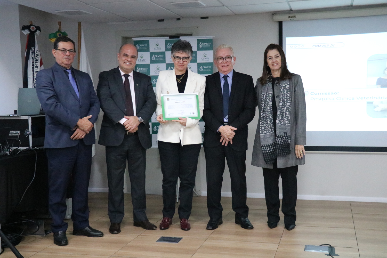No palco, os membros da Diretoria Executiva do CRMV-SP posam ao lado de uma presidente de Comissão Técnica homenageada com certificado em reconhecimento ao trabalho desempenhado.