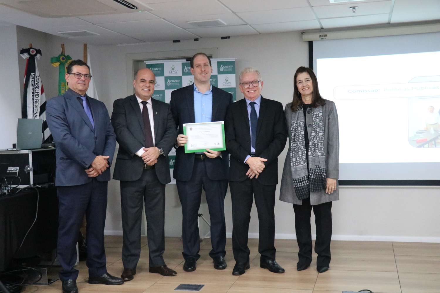 No palco, os membros da Diretoria Executiva do CRMV-SP posam ao lado de um presidente de Comissão Técnica homenageado com certificado em reconhecimento ao trabalho desempenhado.