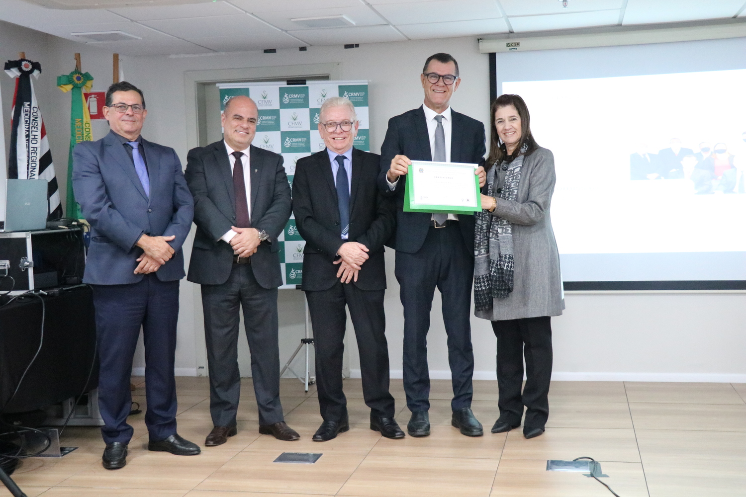 No palco, os membros da Diretoria Executiva do CRMV-SP posam ao lado de um presidente de Comissão Técnica homenageado com certificado em reconhecimento ao trabalho desempenhado.