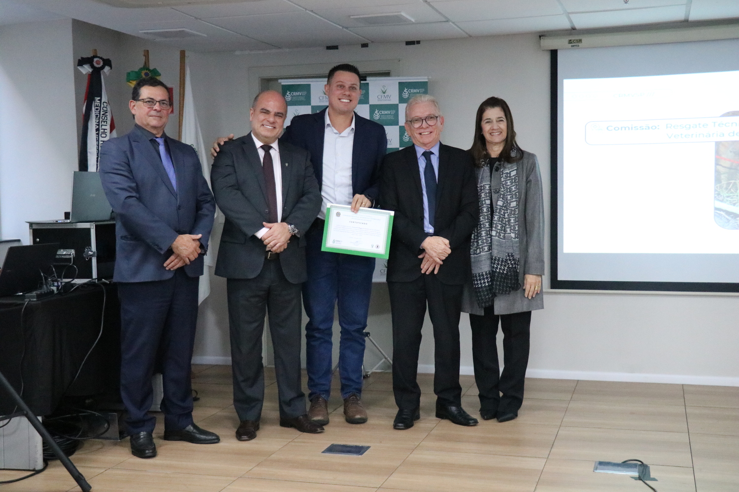 No palco, os membros da Diretoria Executiva do CRMV-SP posam ao lado de um presidente de Comissão Técnica homenageado com certificado em reconhecimento ao trabalho desempenhado.