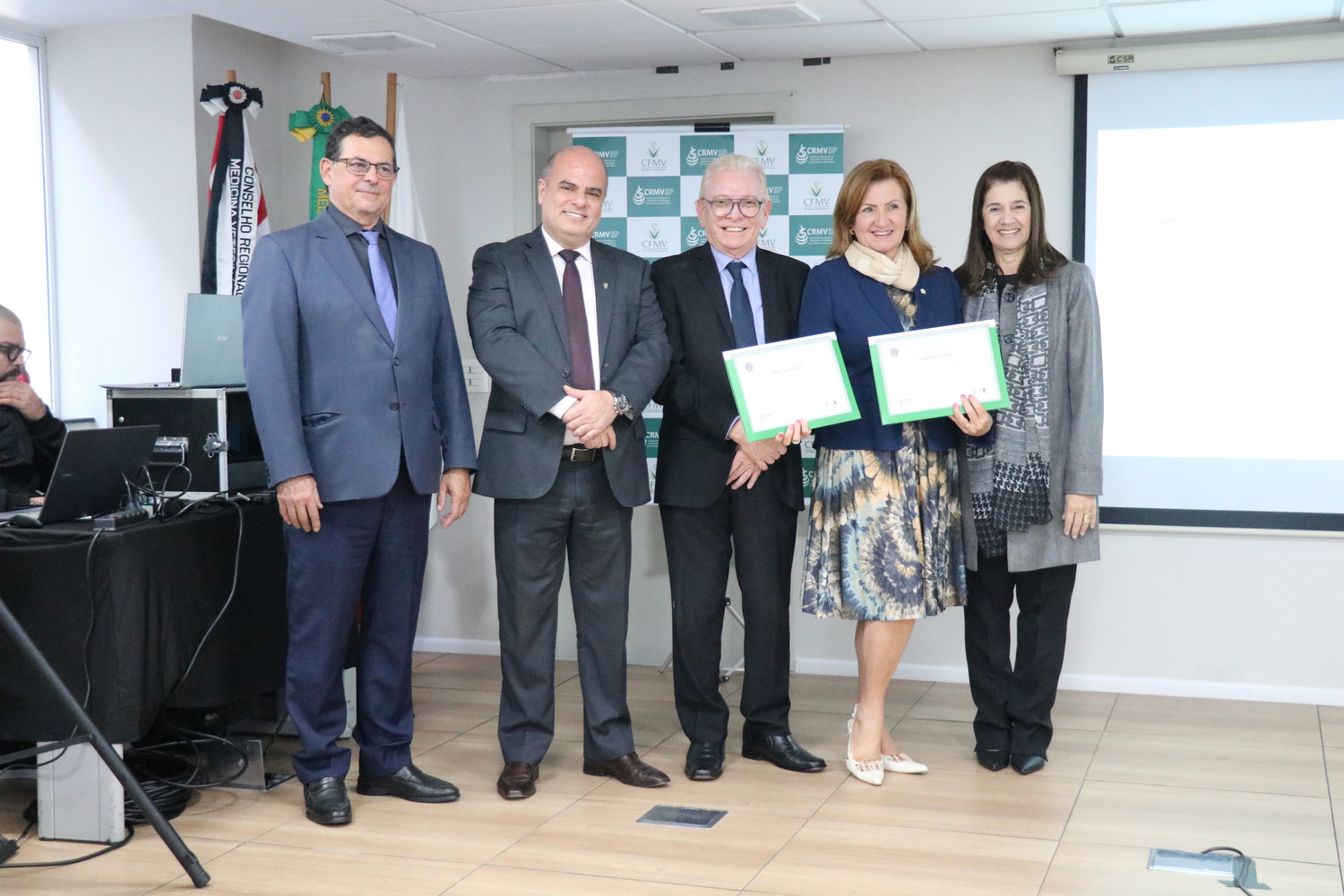 No palco, os membros da Diretoria Executiva do CRMV-SP posam ao lado de uma presidente de Comissão Técnica homenageada com certificado em reconhecimento ao trabalho desempenhado.