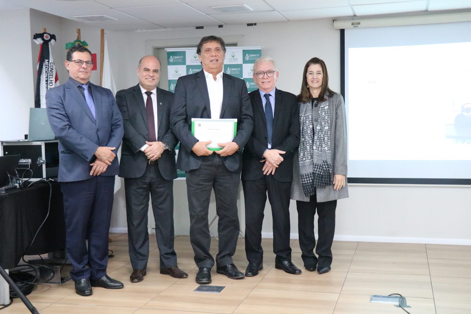 No palco, os membros da Diretoria Executiva do CRMV-SP posam ao lado de um presidente de Comissão Técnica homenageado com certificado em reconhecimento ao trabalho desempenhado.