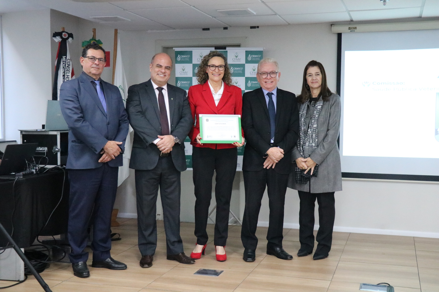 No palco, os membros da Diretoria Executiva do CRMV-SP posam ao lado de uma presidente de Comissão Técnica homenageada com certificado em reconhecimento ao trabalho desempenhado.