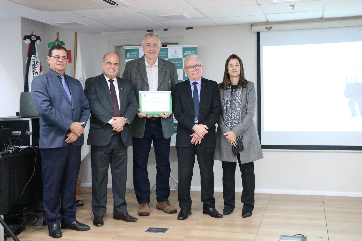No palco, os membros da Diretoria Executiva do CRMV-SP posam ao lado de um presidente de Comissão Técnica homenageado com certificado em reconhecimento ao trabalho desempenhado.