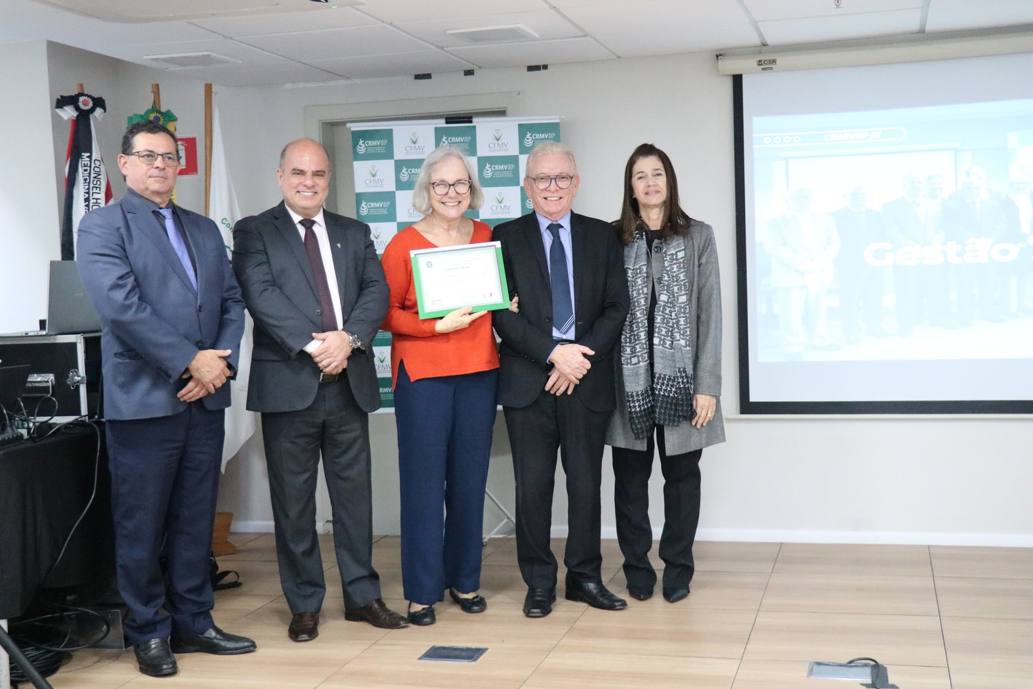 No palco, os membros da Diretoria Executiva do CRMV-SP posam ao lado de conselheira da autarquia homenageada pelo trabalho desempenhado em suas funções.