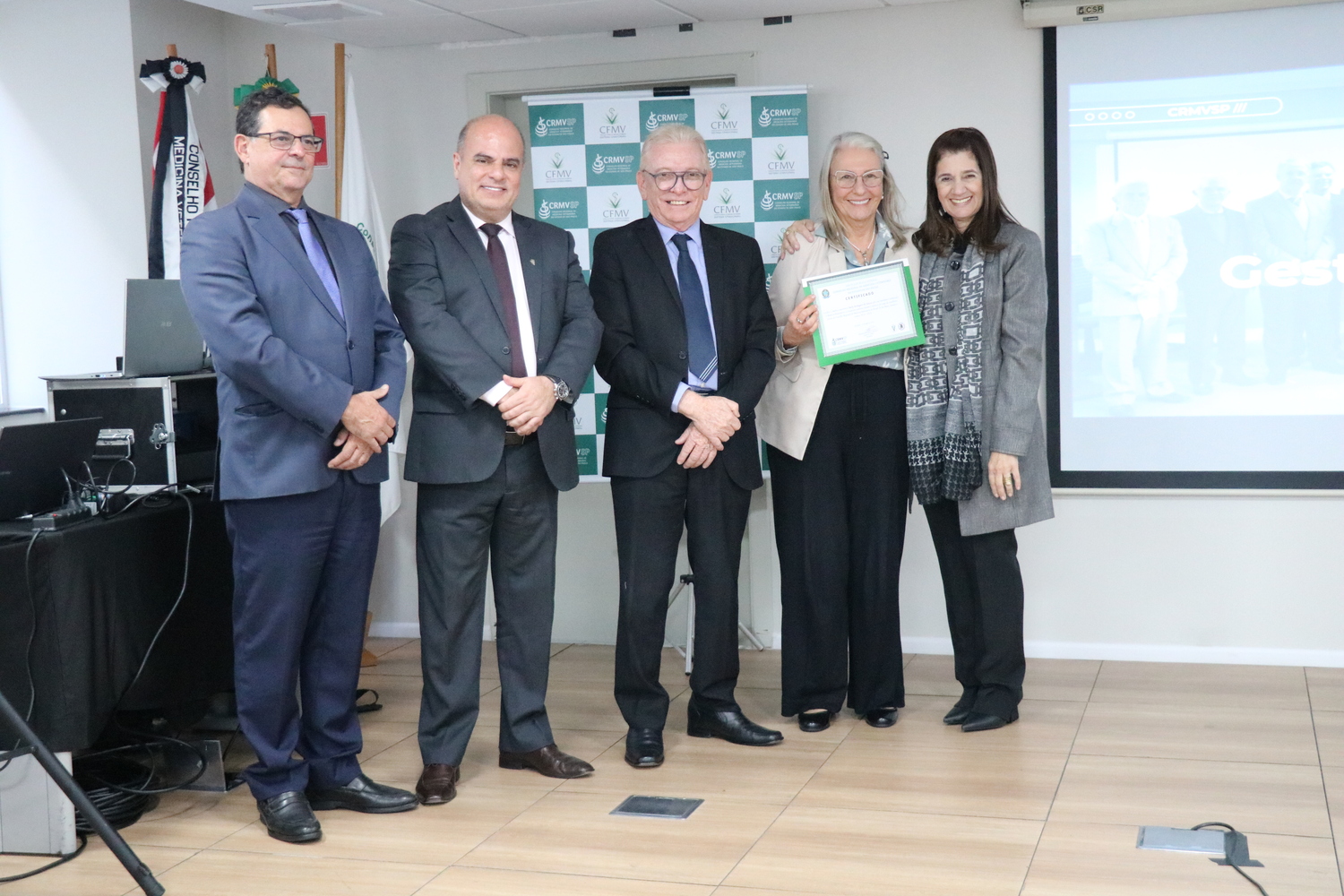No palco, os membros da Diretoria Executiva do CRMV-SP posam ao lado de conselheira da autarquia homenageada pelo trabalho desempenhado em suas funções.