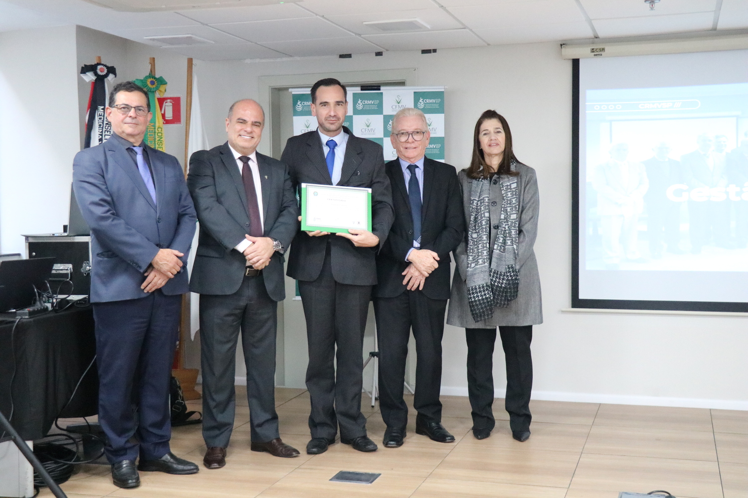No palco, os membros da Diretoria Executiva do CRMV-SP posam ao lado de conselheiro da autarquia homenageado pelo trabalho desempenhado em suas funções.