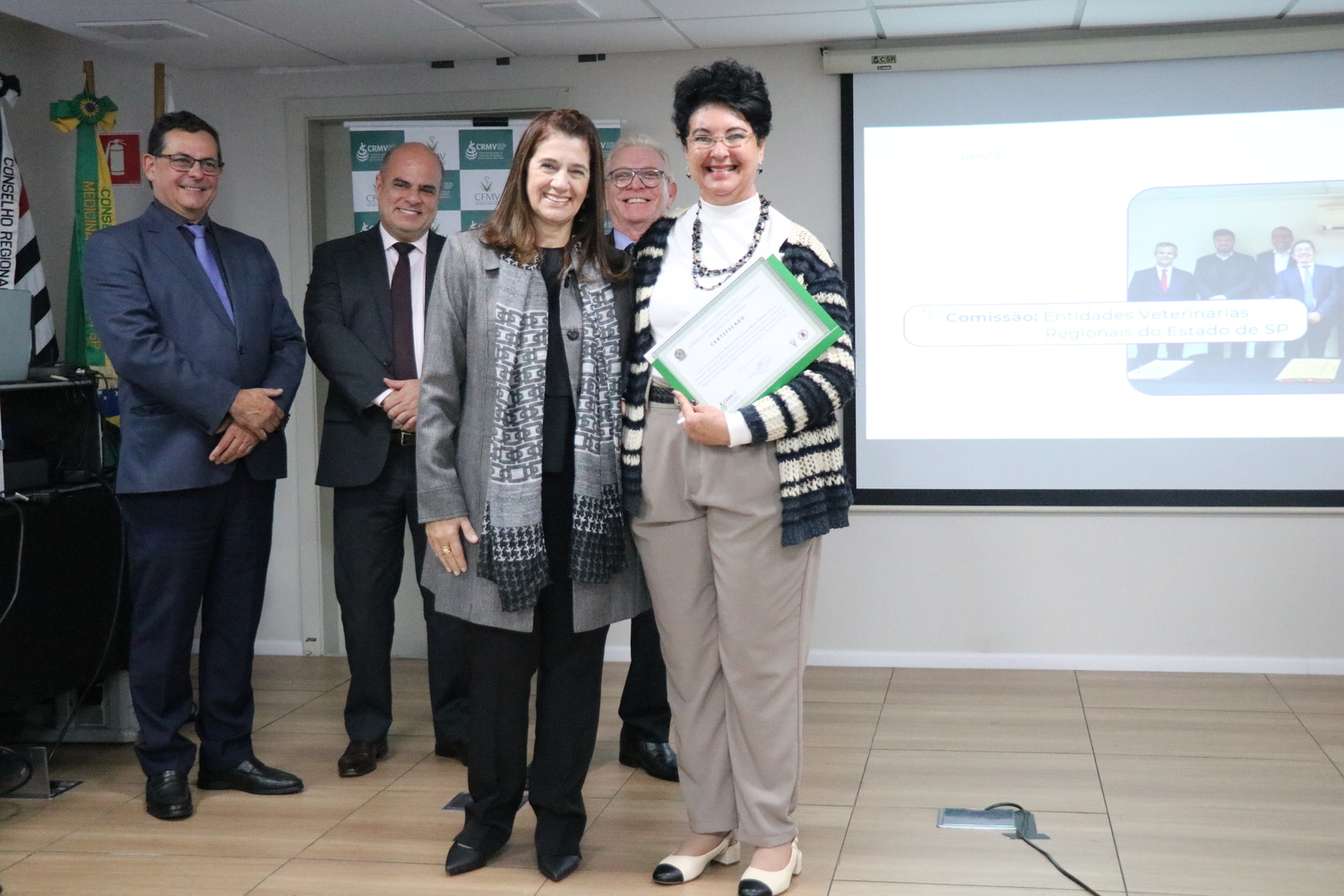 A tesoureira do CRMV-SP entrega certificado para uma presidente de Comissão, ao fundo os outros membros da Diretoria Executiva do Conselho.