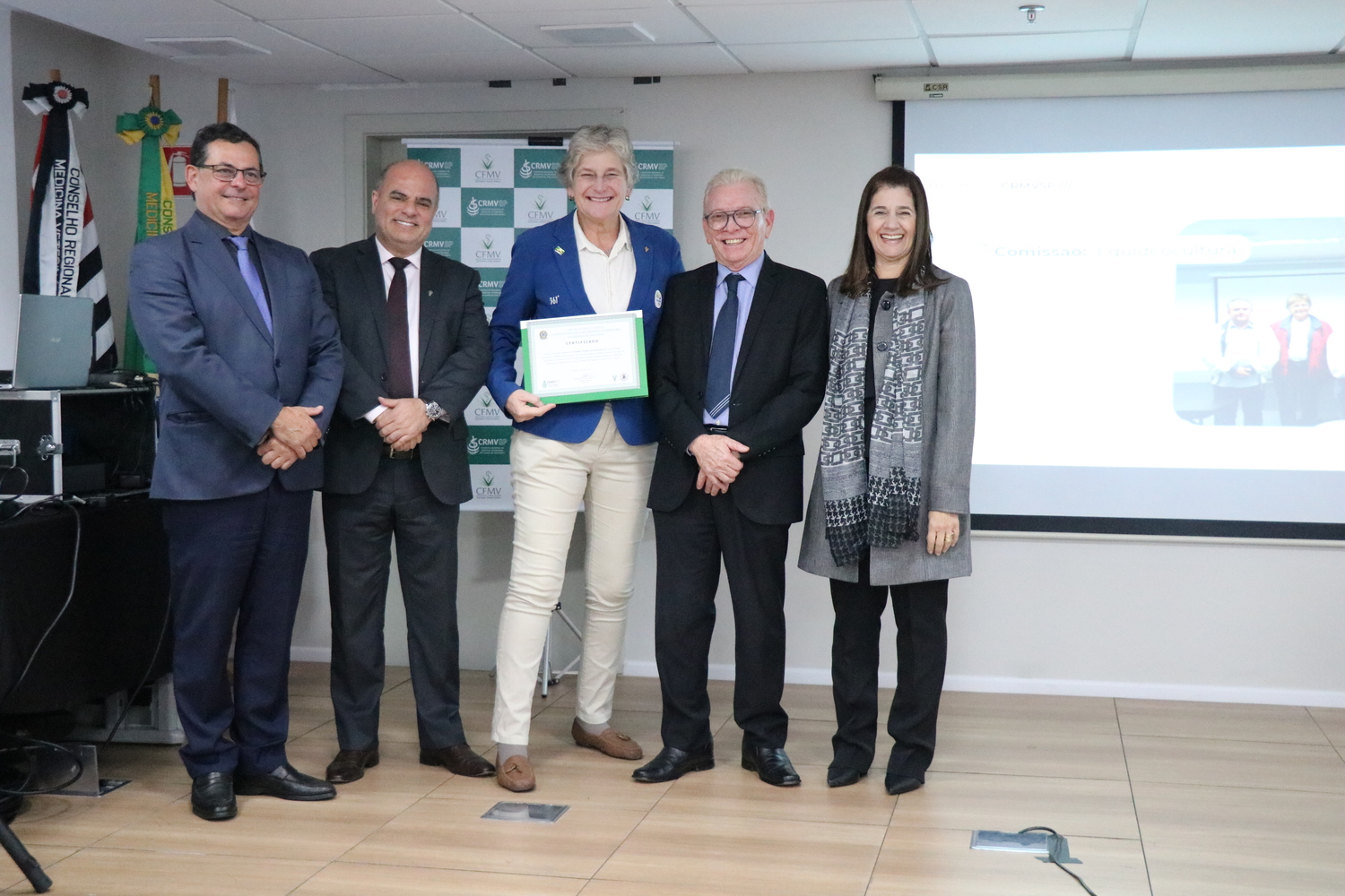 No palco, os membros da Diretoria Executiva do CRMV-SP posam ao lado de uma presidente de Comissão Técnica homenageada com certificado em reconhecimento ao trabalho desempenhado.