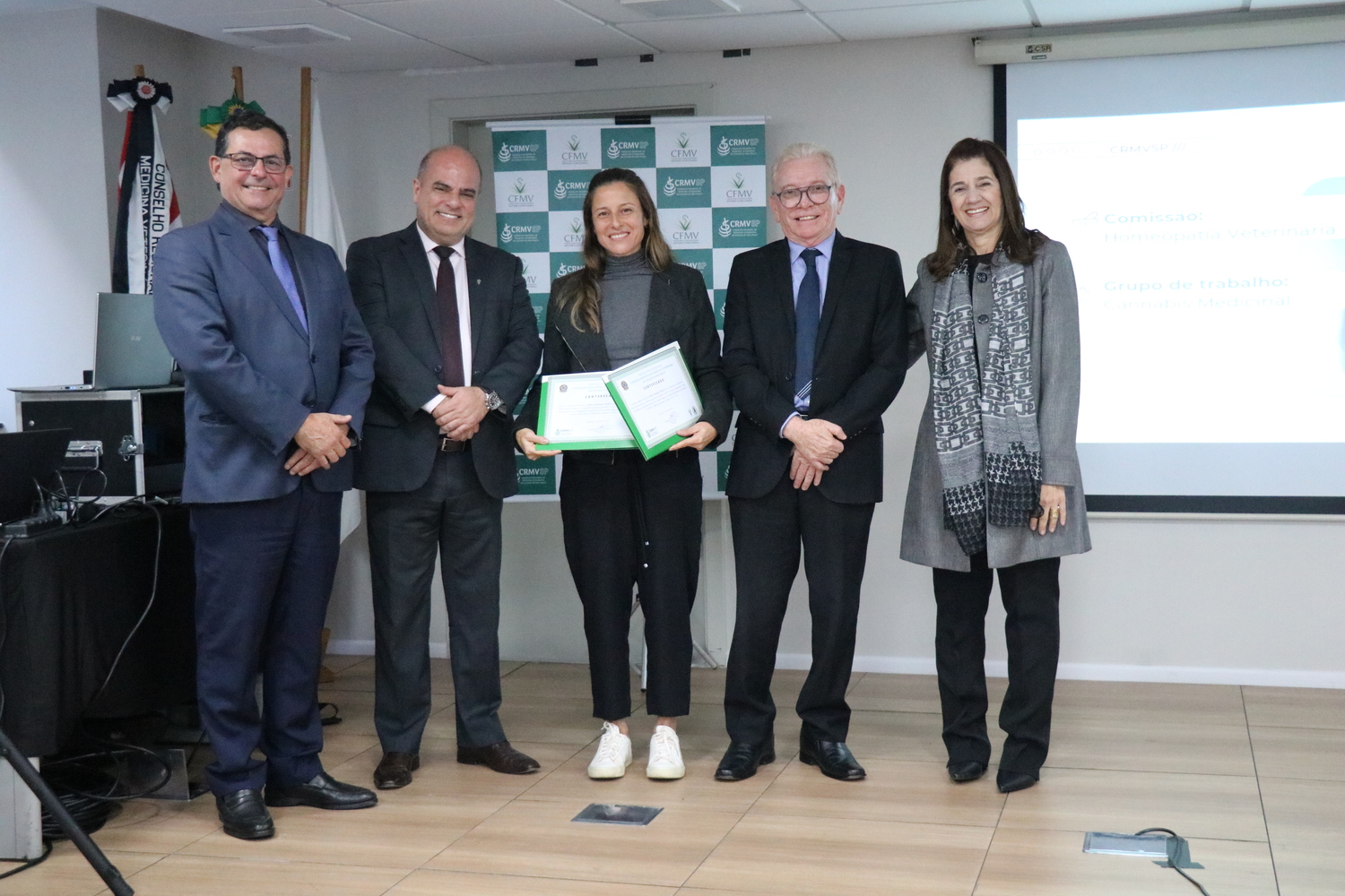 No palco, os membros da Diretoria Executiva do CRMV-SP posam ao lado de uma presidente de Comissão Técnica homenageada com certificado em reconhecimento ao trabalho desempenhado.