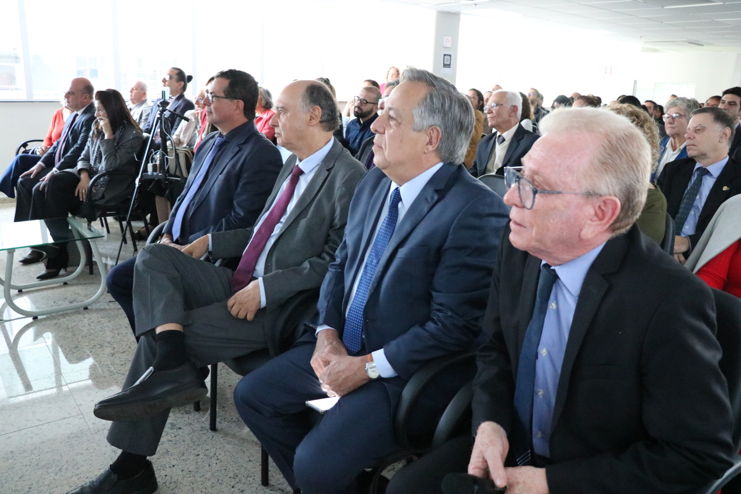 No auditório, o presidente do CRMV-SP está sentado ao lado de ex-presidente CRMV-SP e do vice-presidente do CFMV, eles assistem um vídeo em homenagem ao presidente do CRMV-SP.