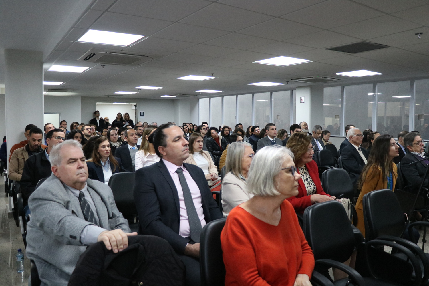 Auditório lotado, imagem da plateia, formada por homens e mulheres.