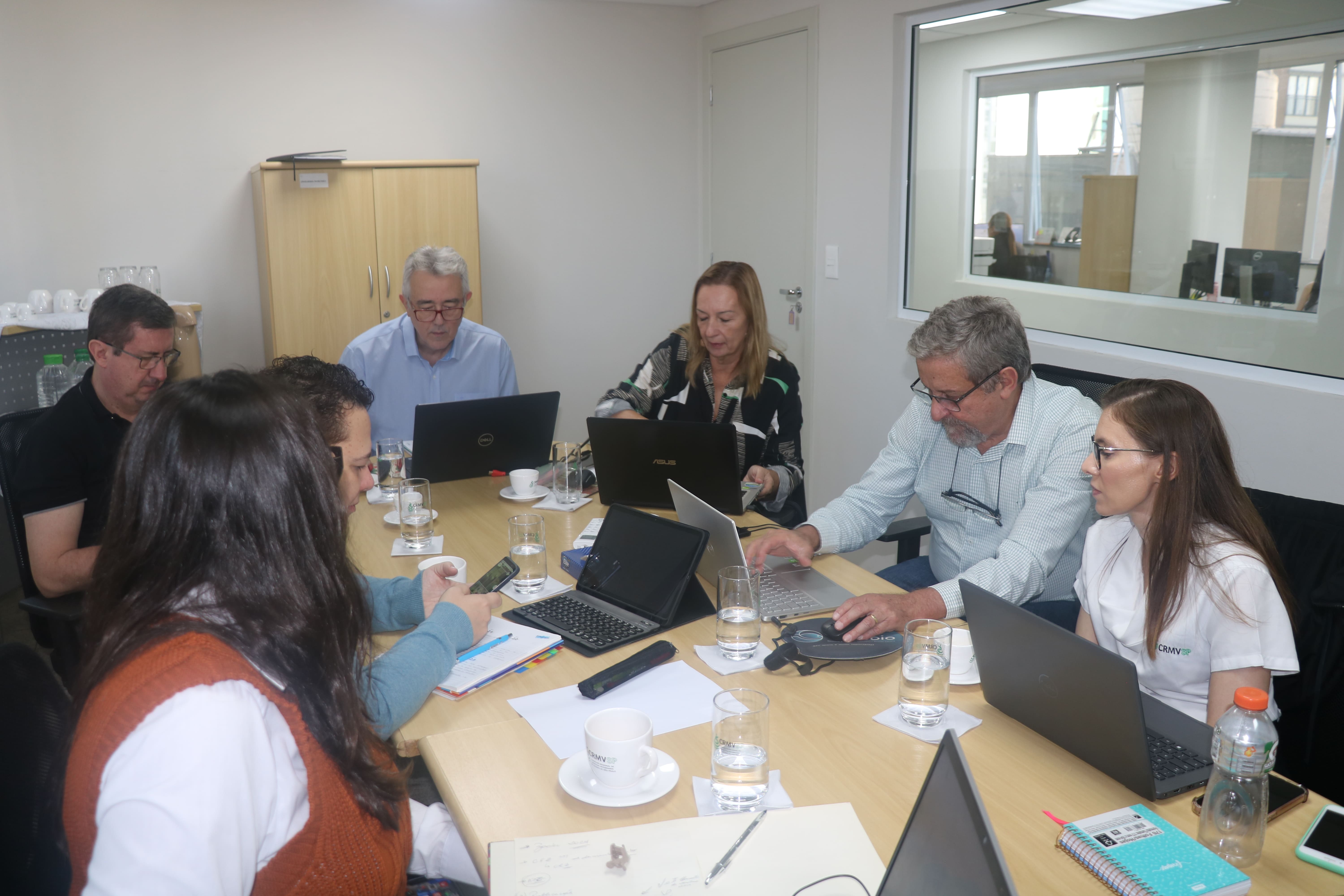 Pessoas reunidas ao redor de uma mesa retangular em reunião.
