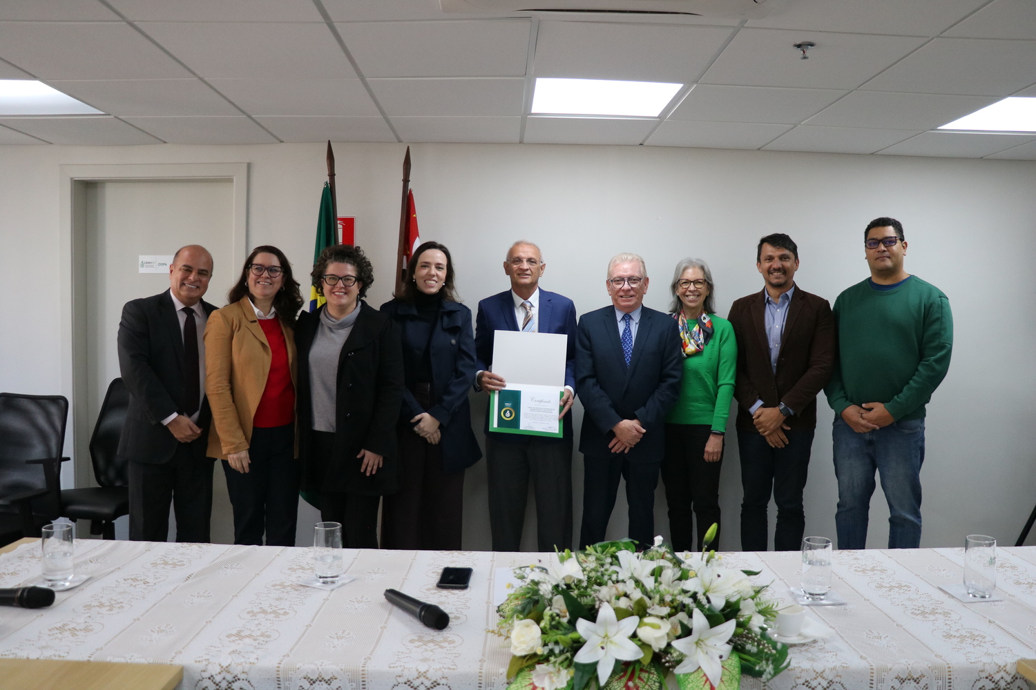 Nove pessoas, entre homens e mulheres, entre eles membros da Diretoria Executiva do CRMV-SP e representantes da FMVZ-USP com o certificado recebido.
