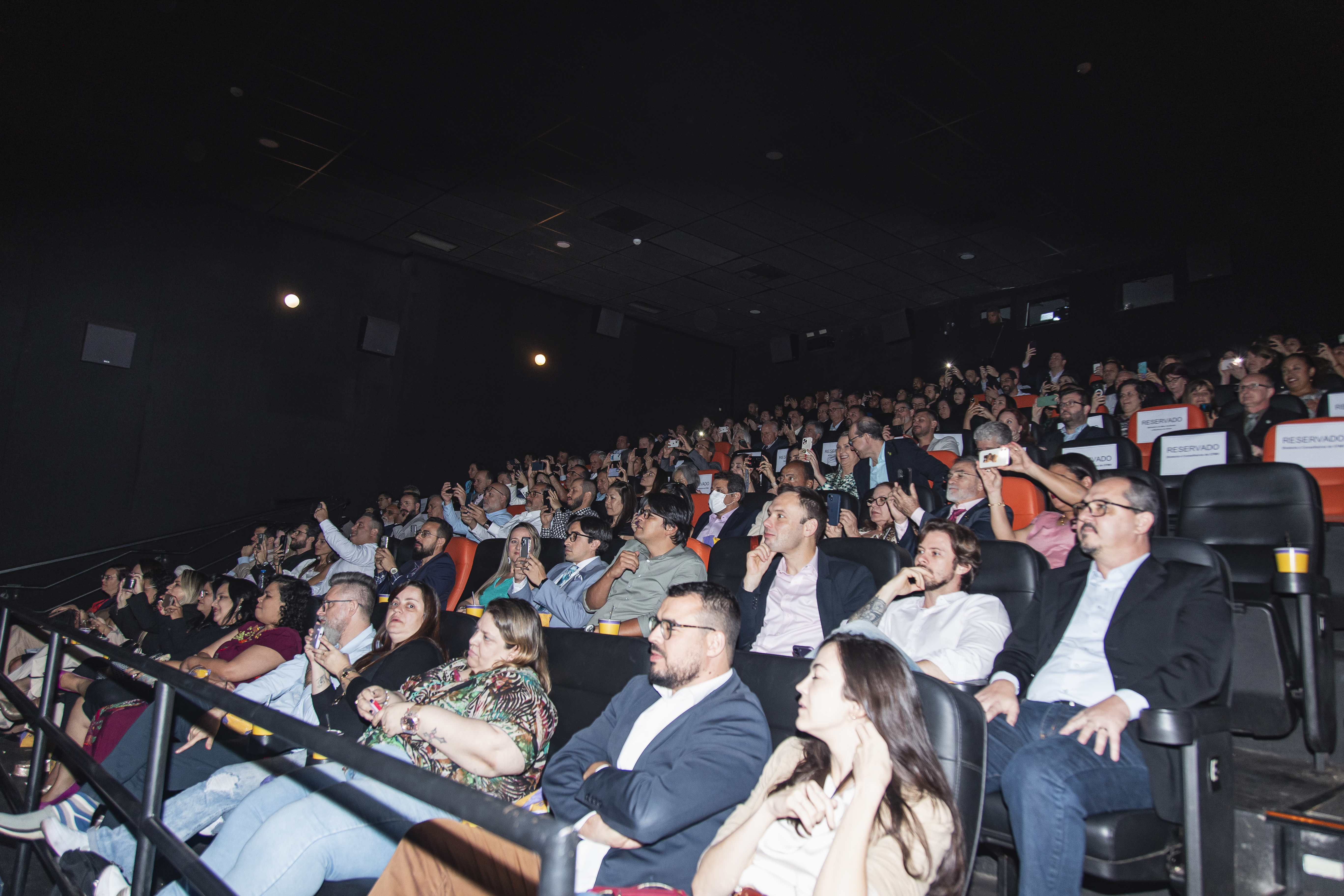 Pessoas sentadas numa sala de cinema assistindo uma apresentação.