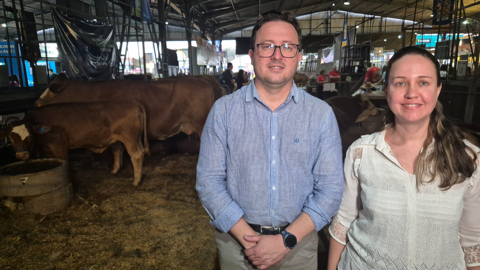 Homem ao lado de mulher em primeiro plano e bois atrás.