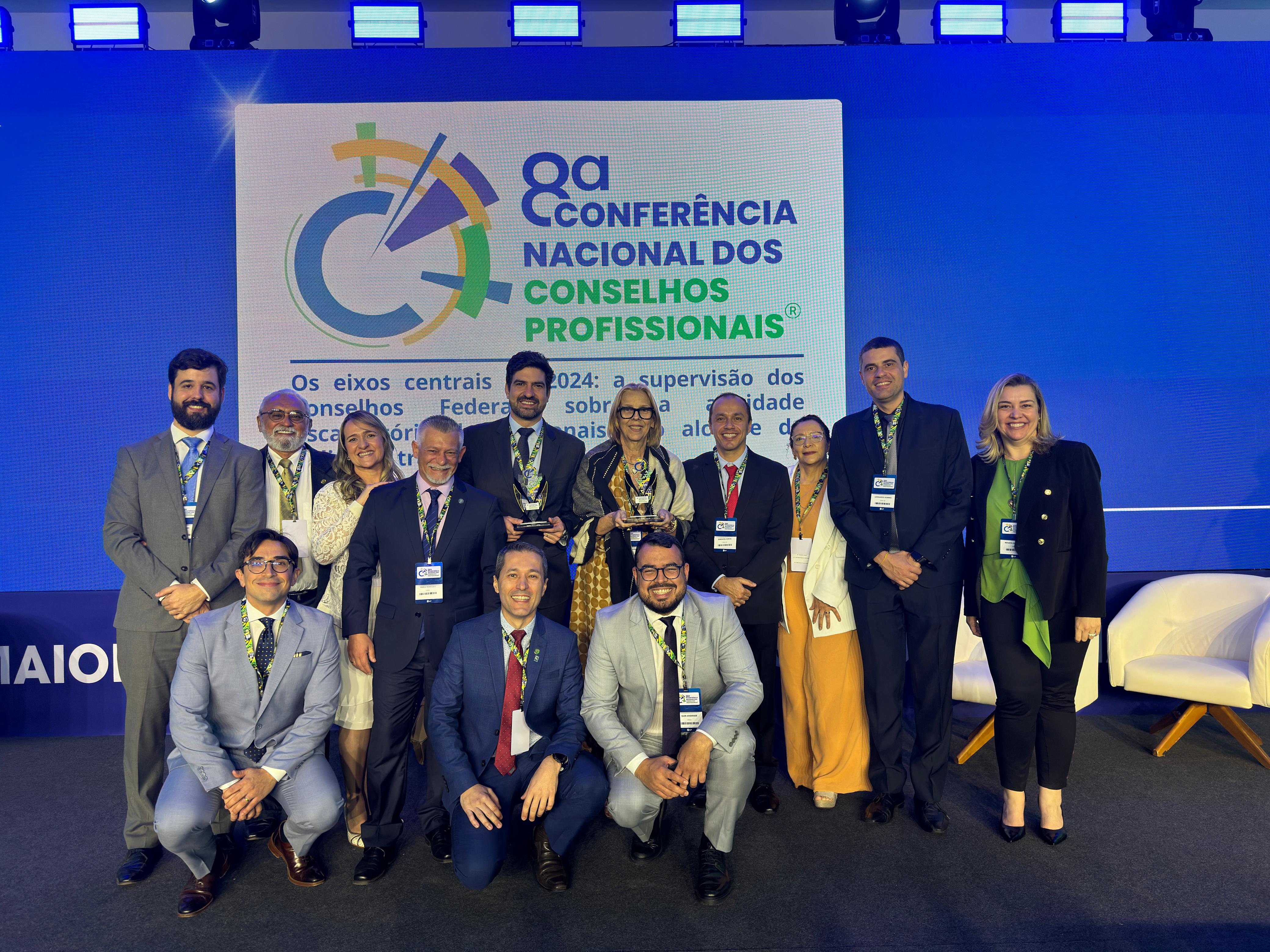 Pessoas pousando para foto com um prêmio na oitava conferência nacional dos Conselhos Profissionais.