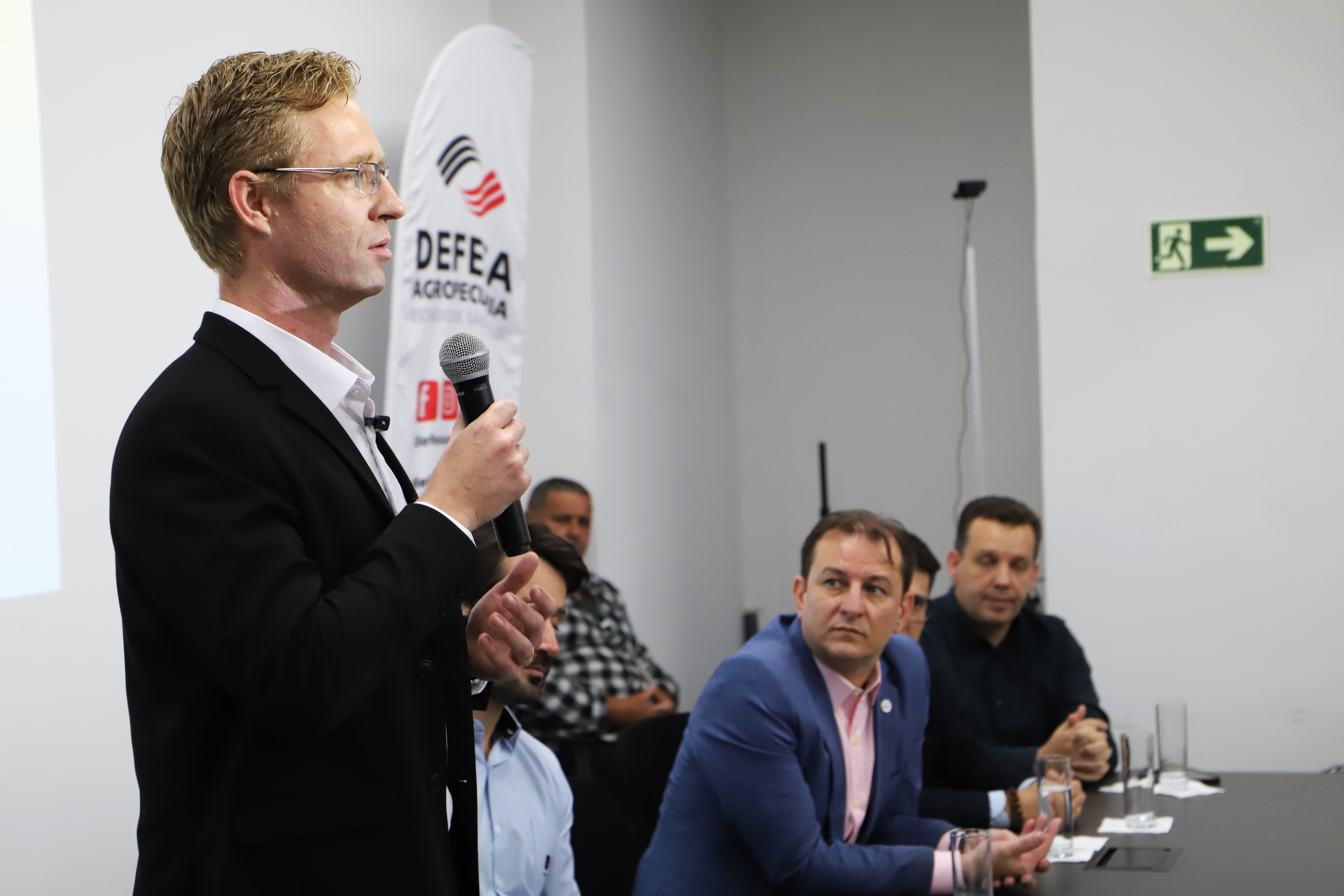 Homem de perfil segurando microfone com uma só mão discursando.