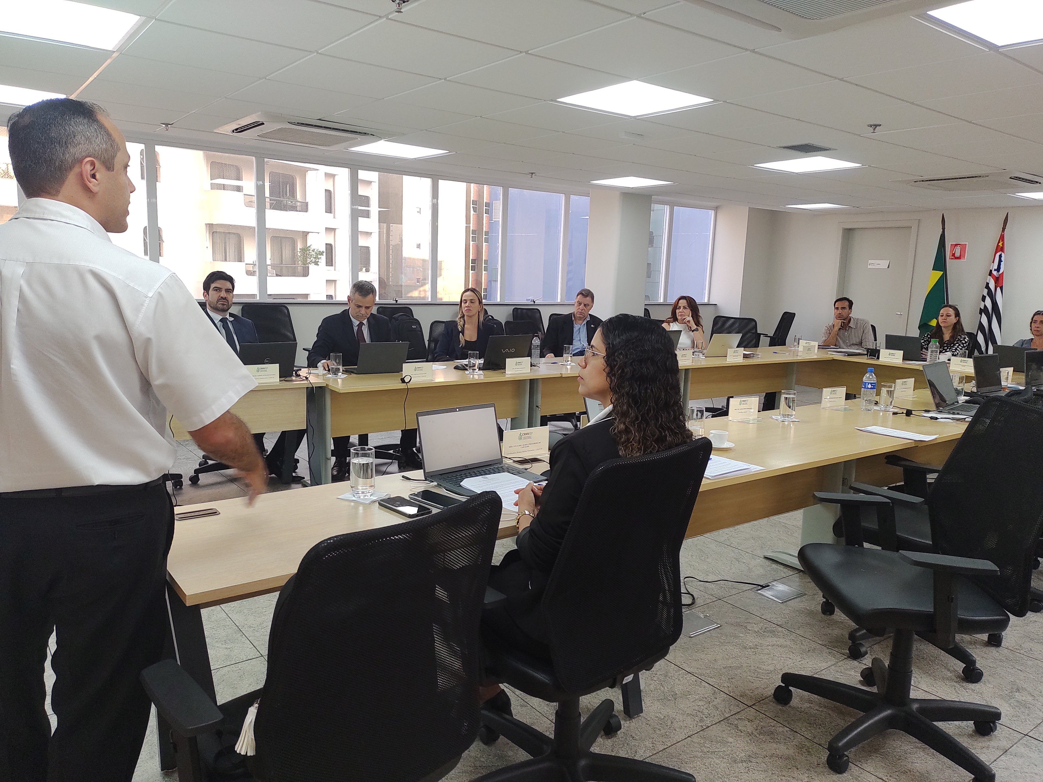 Pessoas na reunião do plenário vendo alguém com microfone na mão falar.