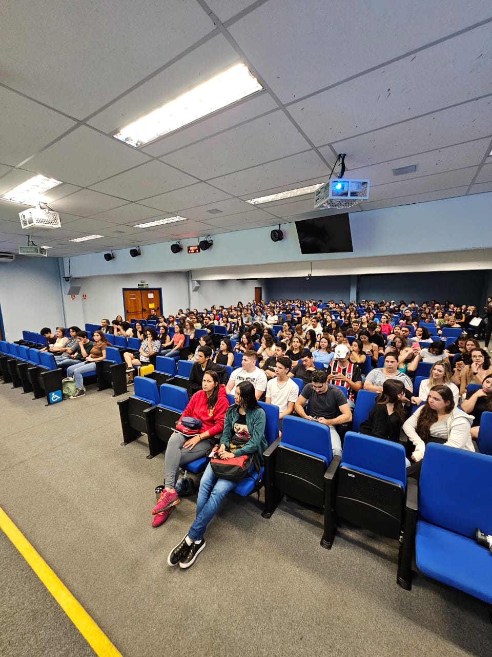 Auditório lotado de pessoas assistindo a palestra.