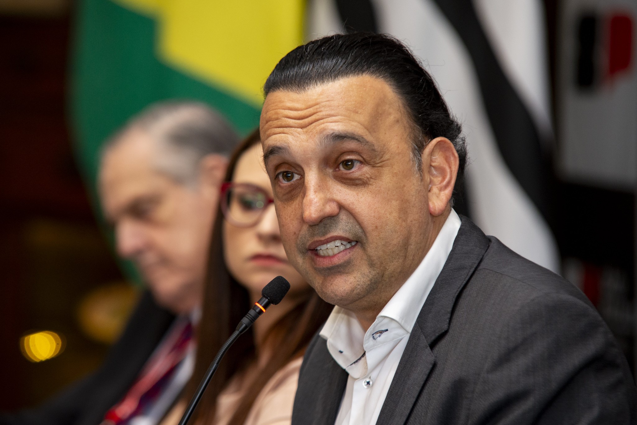 Homem em foco falando ao microfone.