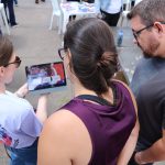 Pessoa mostrando imagens relacionadas a caravana da saúde em um tablet enquanto outros observam.
