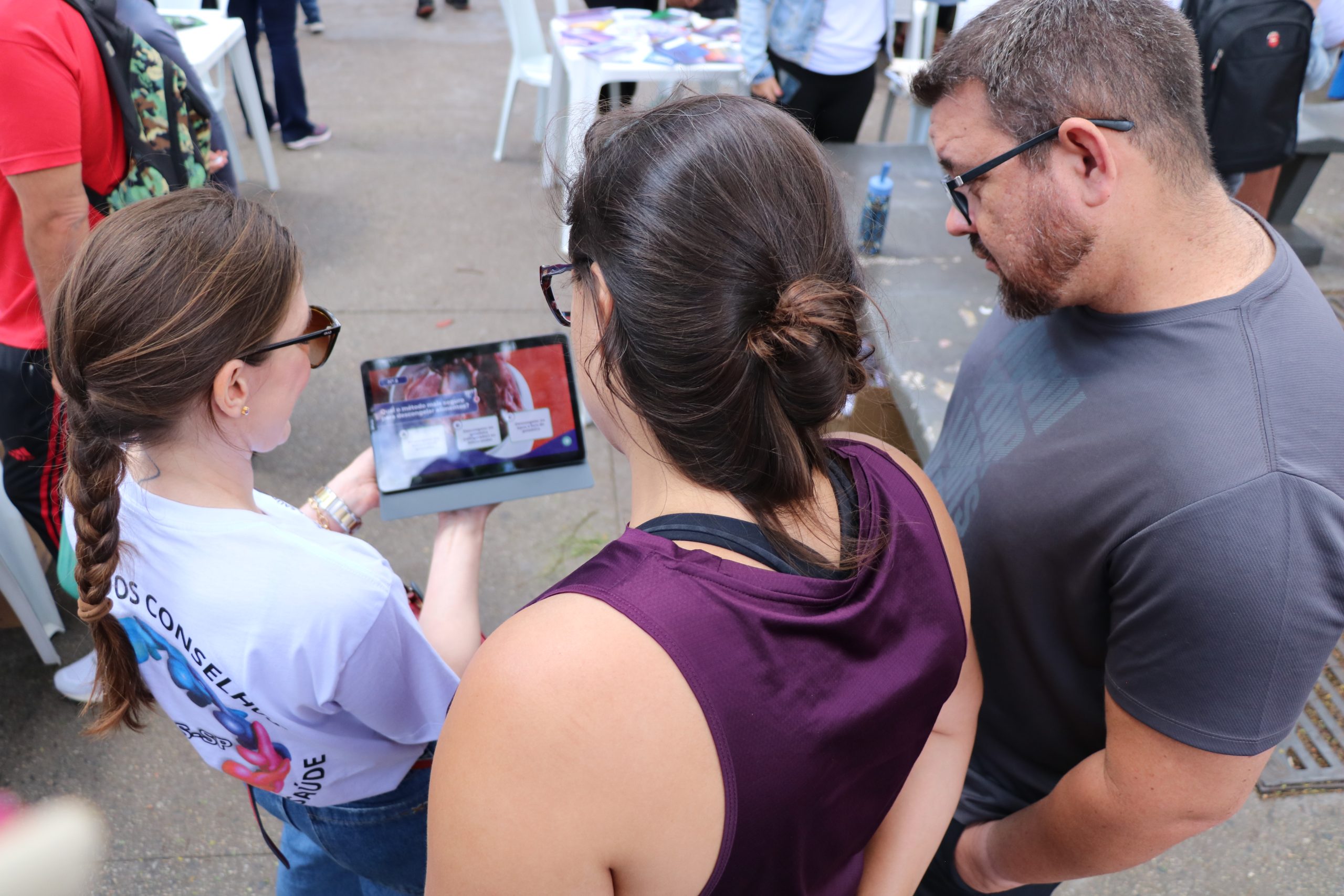 Pessoa mostrando imagens relacionadas a caravana da saúde em um tablet enquanto outros observam.