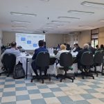 Pessoas sentadas em reunião de costas viradas para a câmera.